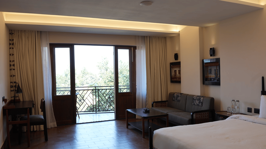 A hotel room interior featuring a bed, a seating area, and open glass doors leading to a balcony at Hotel Sonar Bangla, Ajodhya Hills.