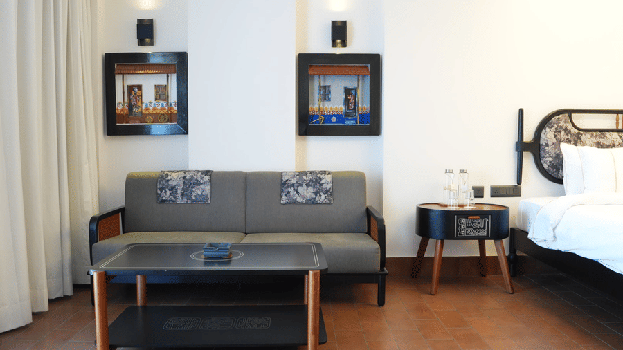 A hotel room featuring a grey sofa, a black coffee table, 2 framed wall pictures, and a bed at Hotel Sonar Bangla, Ajodhya Hills.