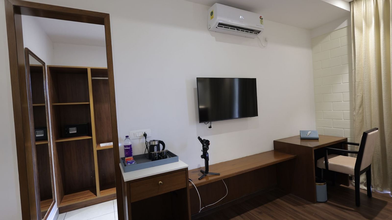 A bedroom with TV, AC and water bottle and kettle on the table at Trishvam Symphony, Krishnagiri.