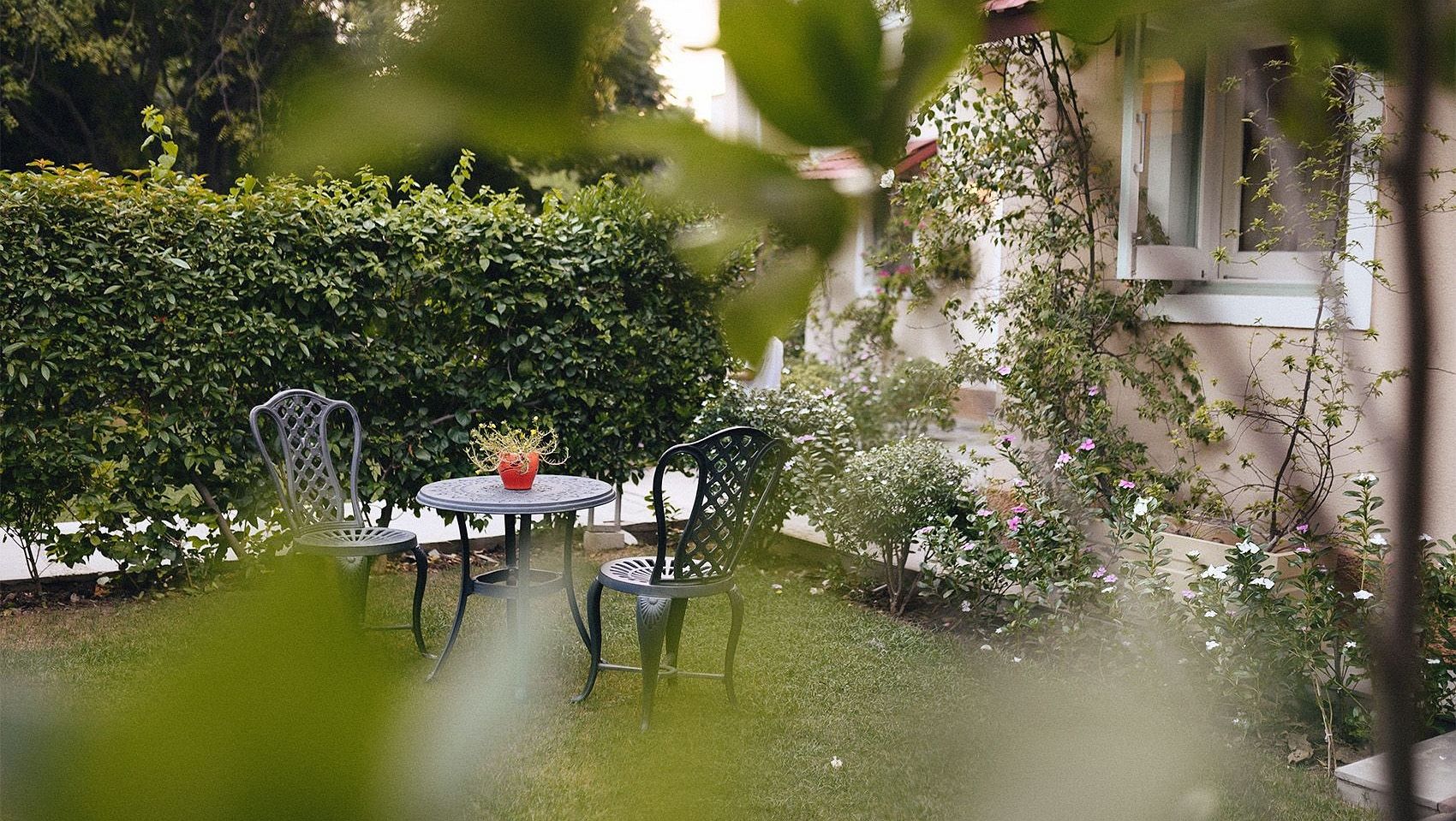 A garden view at Karma Chalets showing a pond, outdoor table and chairs, and green foliage.