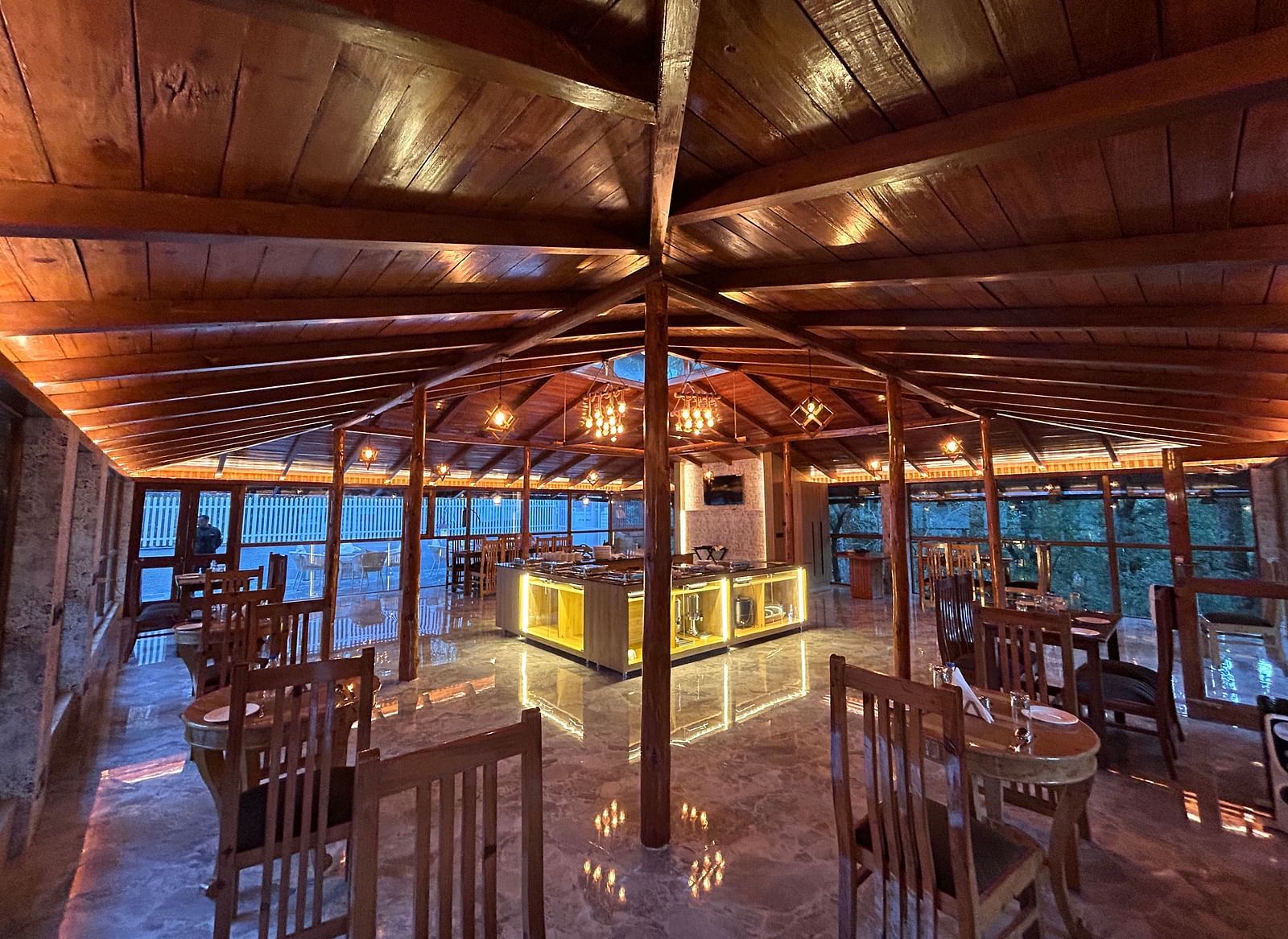 An image of the restaurant at DLS The Emerald, Nainital with wooden interiors along with chairs and tables and the area is lit with bright lighting