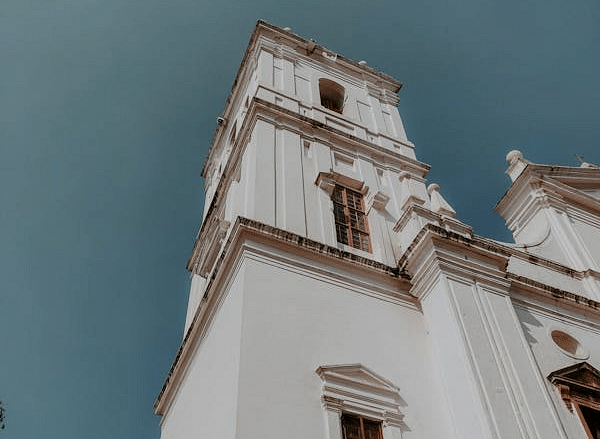 A tall white church with classical architectural details, standing against a bright blue sky.