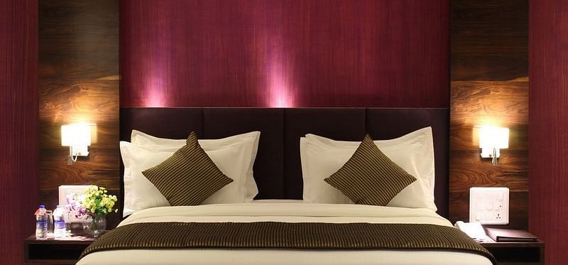 A room showcases a king size bed with a dark purple headboard, bedside tables with lamps, and elegant bedding.
