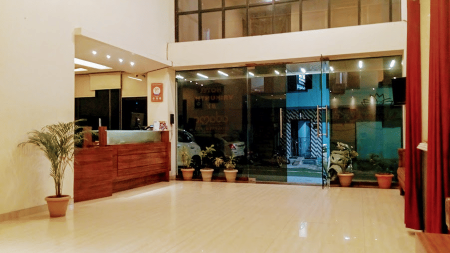 Bright hotel lobby area featuring a wooden front desk counter, a glass entrance doors, and potted plants.