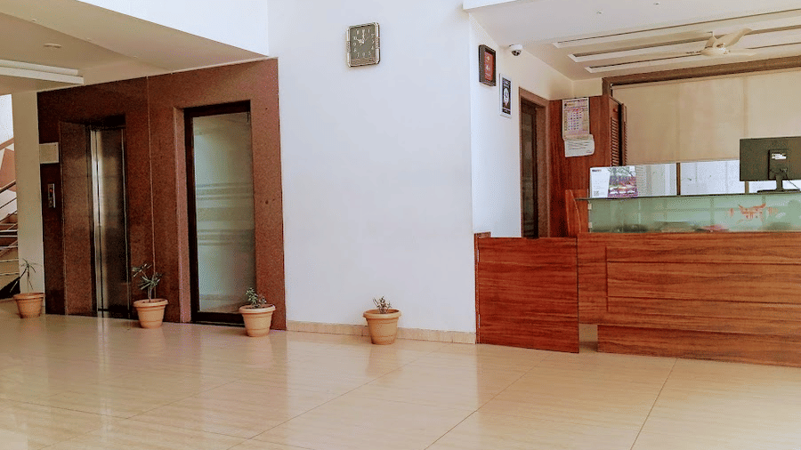  Hotel reception hall showcasing a wooden desk counter, tiled flooring, and a glass-enclosed lift or elevator.