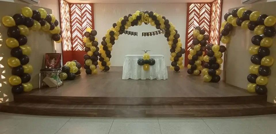 An event space with a decorated stage, balloons, and a white backdrop - Lords Eco Inn Belagavi