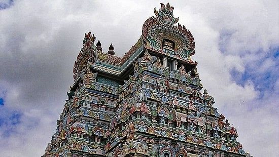 A tall, intricately sculpted temple tower with colourful figures against a cloudy sky.