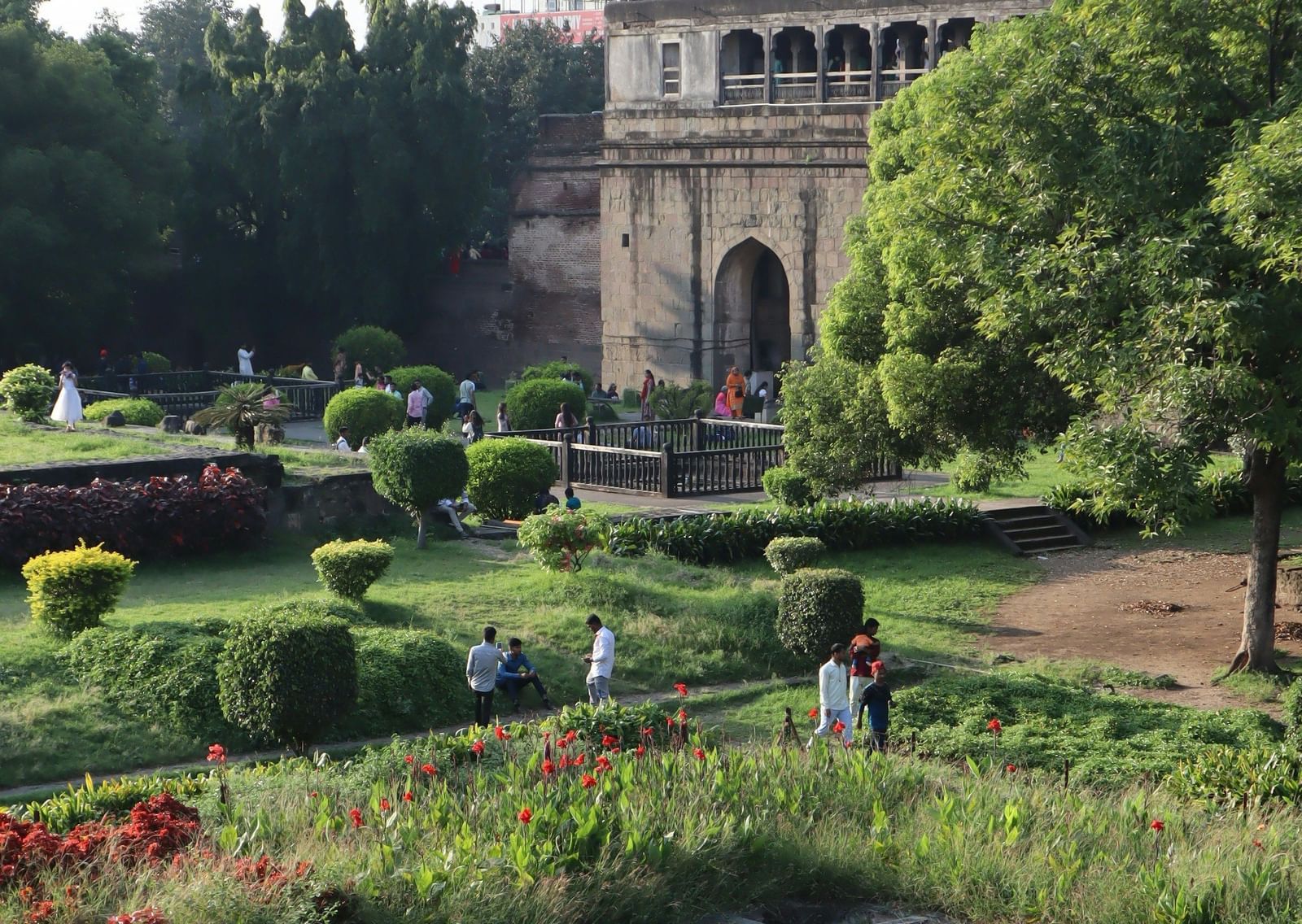 A serene, low-angle view of a traditional Indian building with a garden, featuring a decorative stone pond in the foreground and a larger building in the background.