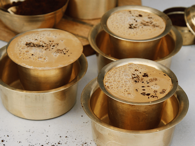 3 metal containers with coffee, placed on a surface, with lids and utensils arranged nearby.