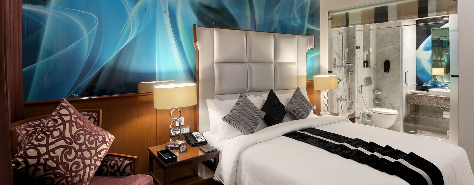 Spacious room with a large bed and cushioned sofa beside it, with a washroom in the background at The Elanza Hotel.