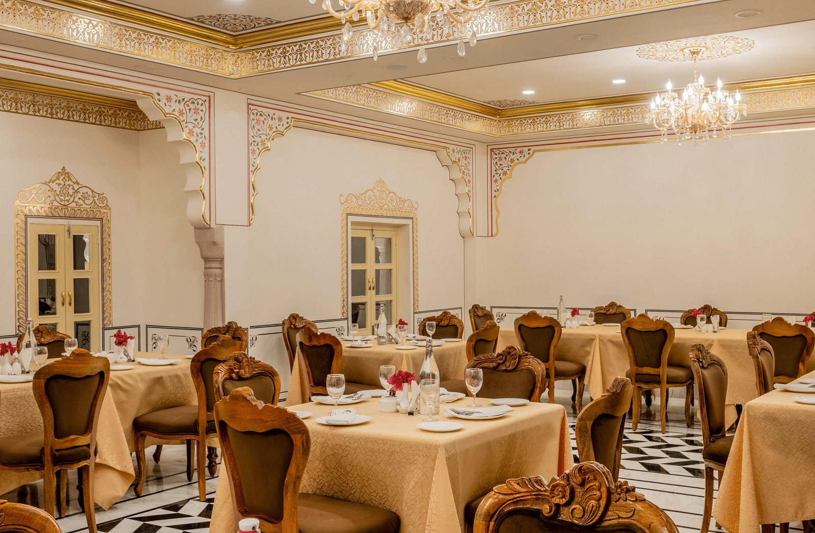 side view image of the dining area with well arranged crockery along with a small flower vase with rose kept in it - Brij Castle, Jaipur