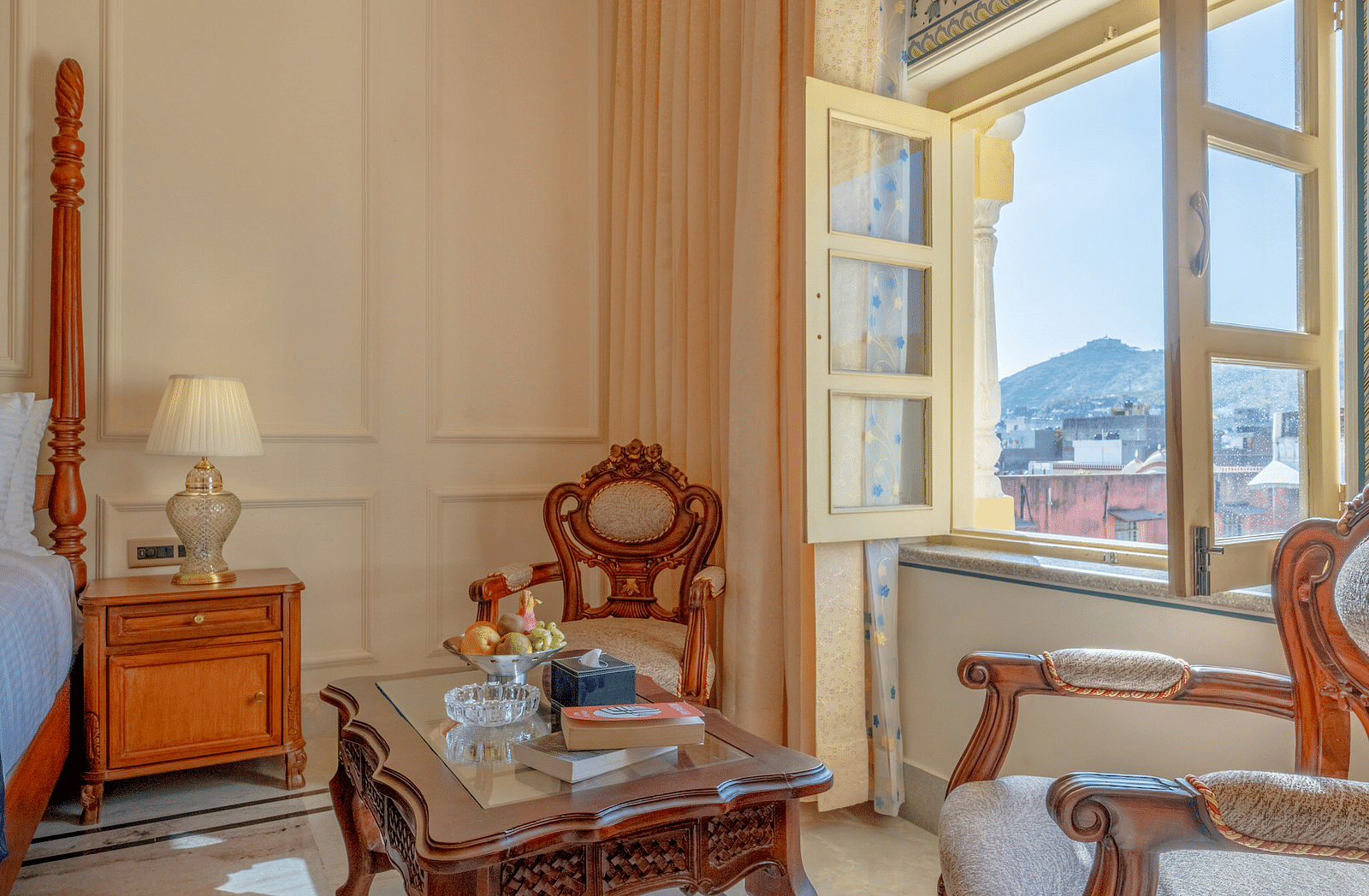 two beautiful wooden armchairs placed in front of a coffee table with open windows - Brij Castle, Jaipur