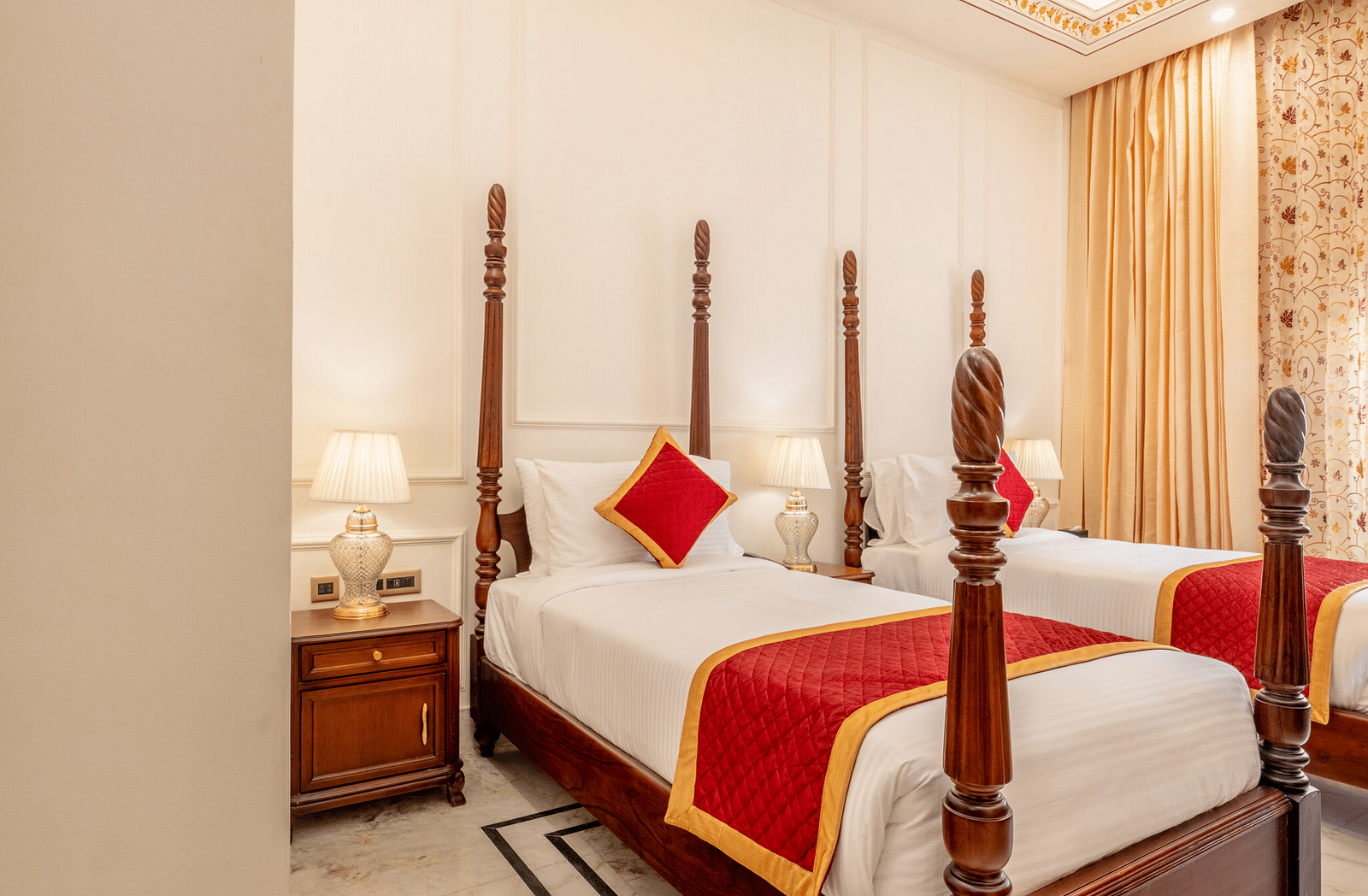 a bedroom with elegant interiors featuring a false ceiling along with a twin bed with bed sides tables beside it - Brij Castle, Jaipur