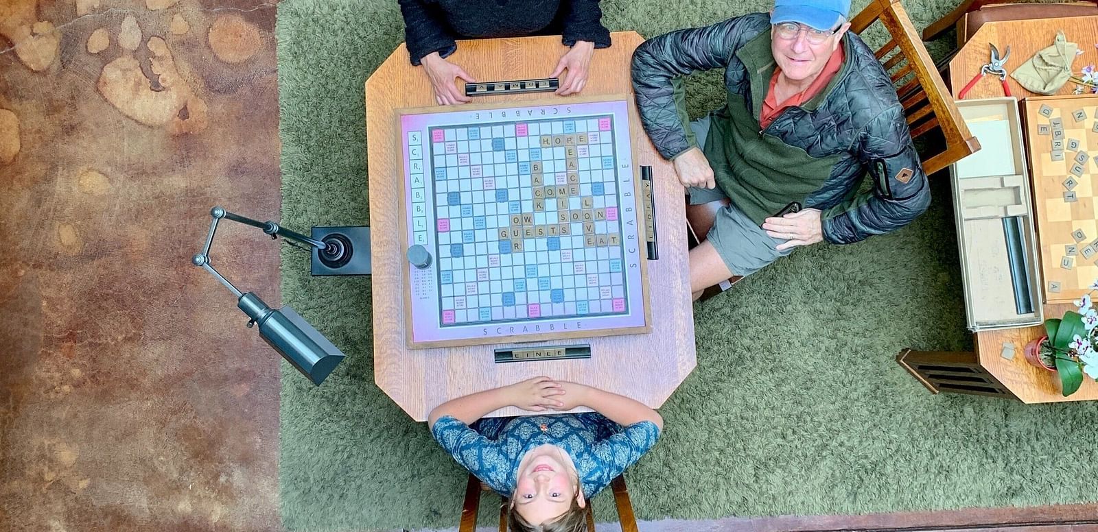 An image of a kid enjoying scrabble board game along with few adults on the table