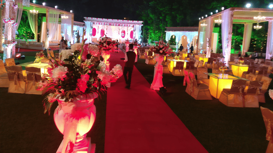 A vibrant outdoor wedding reception is decorated with pink and white flowers and bright lights, with a red carpet leading through the centre - Clarks Avadh, Lucknow