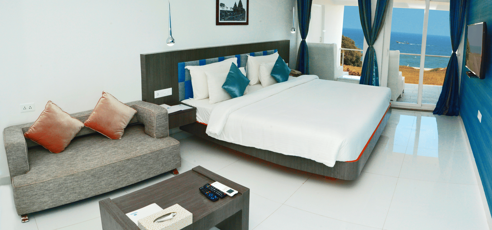 A clean, modern hotel bedroom with a large white bed, dark accent wall, and a small sitting area - Grande Bay Resort & Spa, Mamallapuram