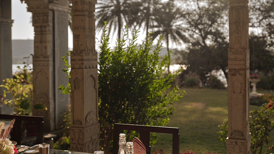 Pillared veranda overlooking palm trees, with a table set with glasses at Dev Shree, Deogarh.