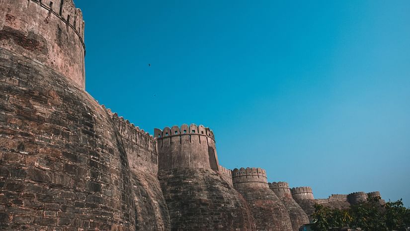 Old tall wall with round like curves perching on the outside, the wall has black  impressions on it under a blue sky 