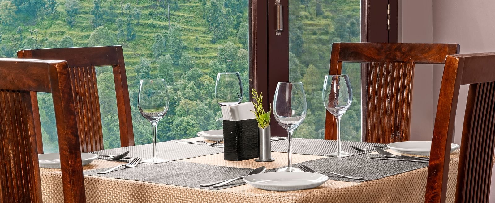 Indoor dining area with a view of terraced hills through large glass windows at BluSalzz Collection - Suvaasa Resort, Ramgarh.