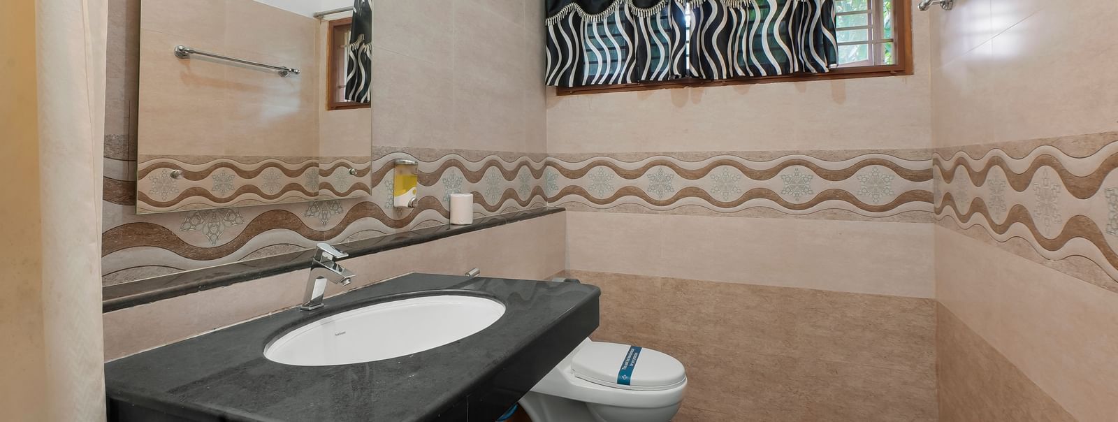 Spacious washroom with a washbasin, a wall-mounted mirror and a western toilet at WOW Bungalow, Yercaud.