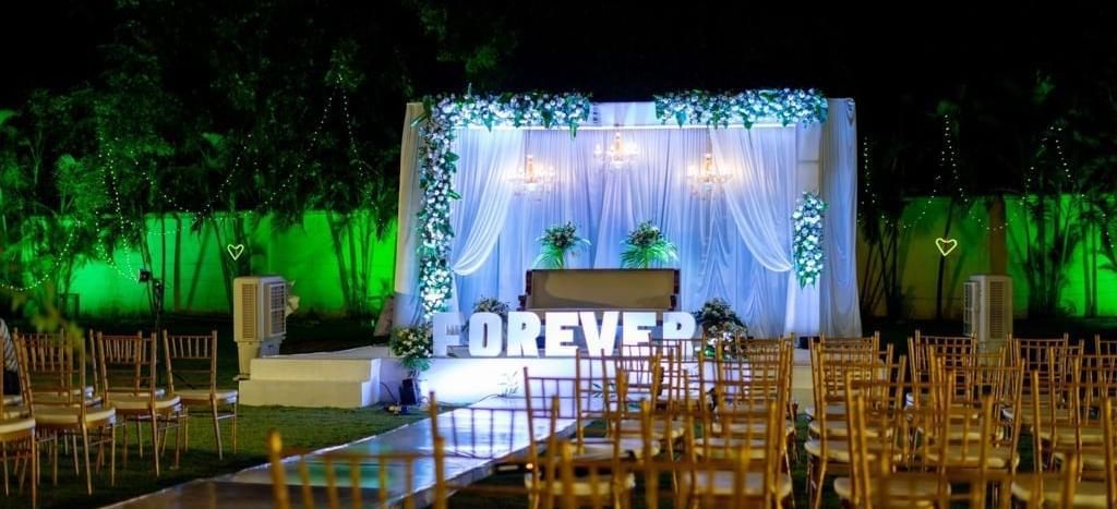 Evening view of outdoor seating facing a floral-lit stage with ‘FOREVER’ signage at Ilara Hotels & Spa, OMR, Chennai