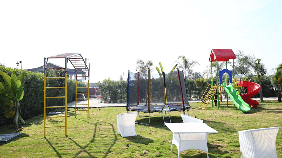 Outdoor grassy playground featuring a trampoline, colourful slides, a jungle gym, and white patio furniture.