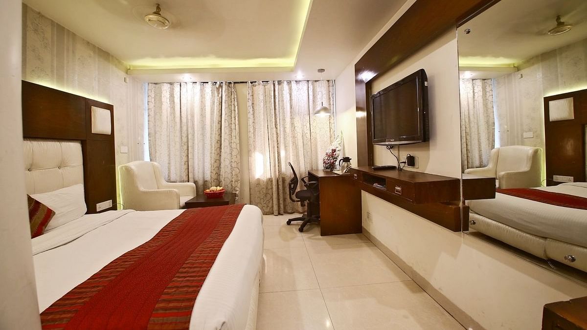 A hotel room with a plush bed, a red runner, a sofa, a TV, and a mirror. - Hotel Diamond Plaza, Chandigarh.