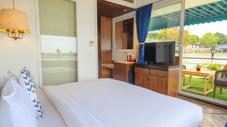 Bright room at Polo Floatel Kolkata with balcony access, bed, white curtains, and a wall-mounted TV.