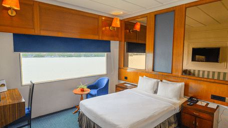 Double bedroom at Polo Floatel Kolkata with blue curtains, wooden paneling, and river-facing window.