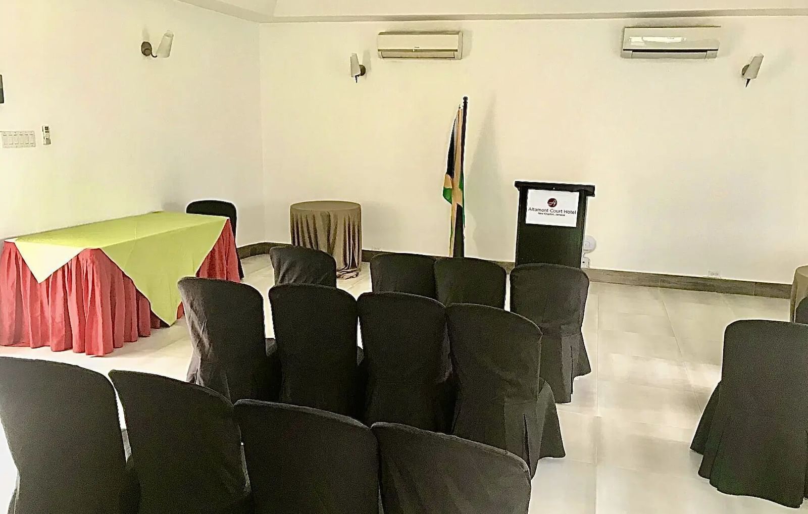 An empty conference room features rows of black chairs facing a table with a television screen and a Jamaican flag | Altamont Court, Jamaica