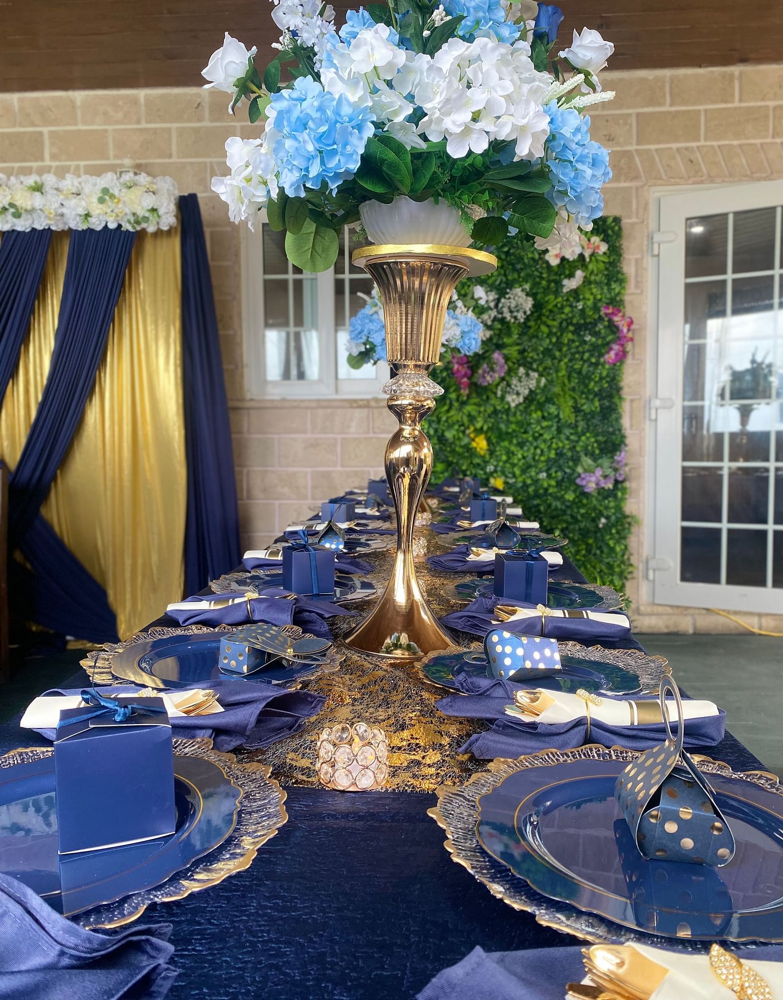 Long banquet table with navy blue napkins, golden cutlery, and tall floral centerpiece | A Stone's Throw Away