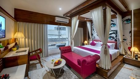 A room with a spacious bed, a small table with chairs, and a window with curtains at Angel Lords Eco Inn Amreli.