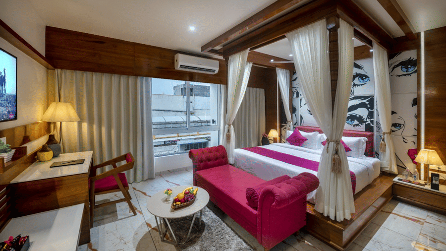 A room with a spacious bed, a small table with chairs, and a window with curtains at Angel Lords Eco Inn Amreli.