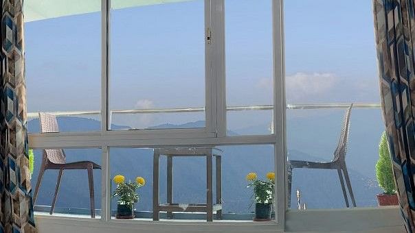 Balcony with two chairs, one table with small plants placed near the chairs and a big glass window at A room with double bed, Framed art work on the wall, TV, Wardrobe, Dustbin, Table and desk with two water bottles on the top at Central Heritage Resort an