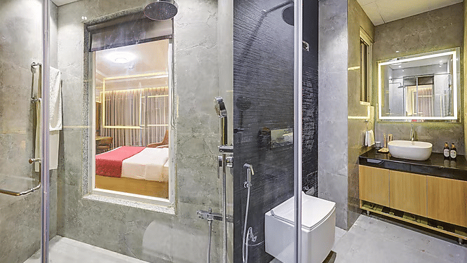 A contemporary bathroom featuring grey tiled walls, a glass-enclosed rain shower, and a back-lit vanity mirror over a sleek sink - Hotel 91 HUDA City Centre, Gurugram