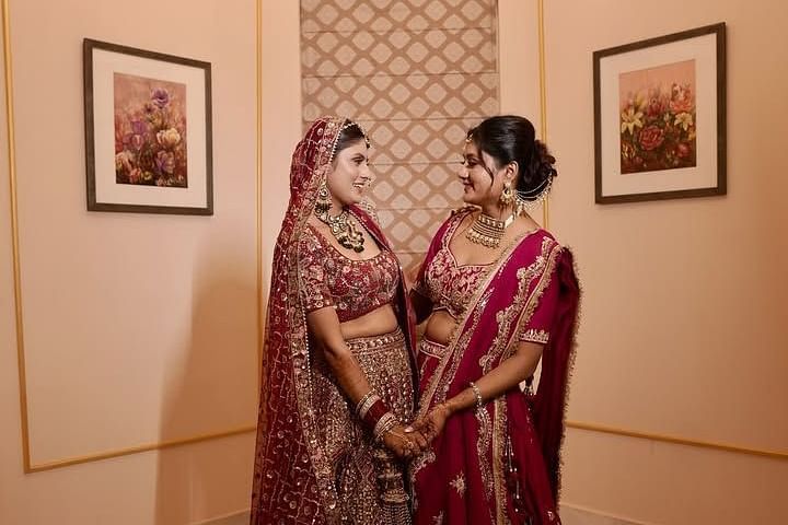 A bride and her bridesmaid in matching lehengas, smiling and holding hands in an elegant indoor setting. - Umaid Palace - A Lakeside Heritage Palace Resort