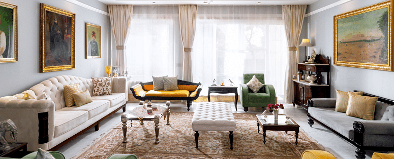 A spacious living room with a mix of modern and classic furniture, including sofas, armchairs, and coffee tables, under a chandelier and with artwork on the walls | Dileep  Kothi, Jaipur