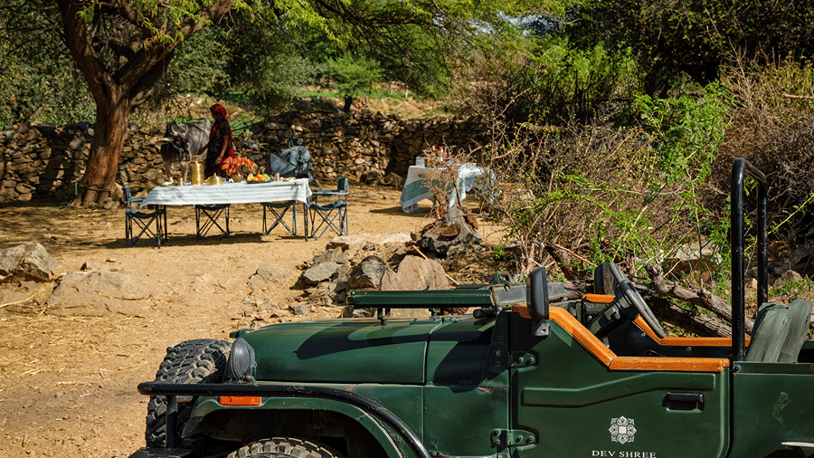 Open-top jeep parked beside an outdoor dining table set up under trees at Dev Shree, Deogarh.