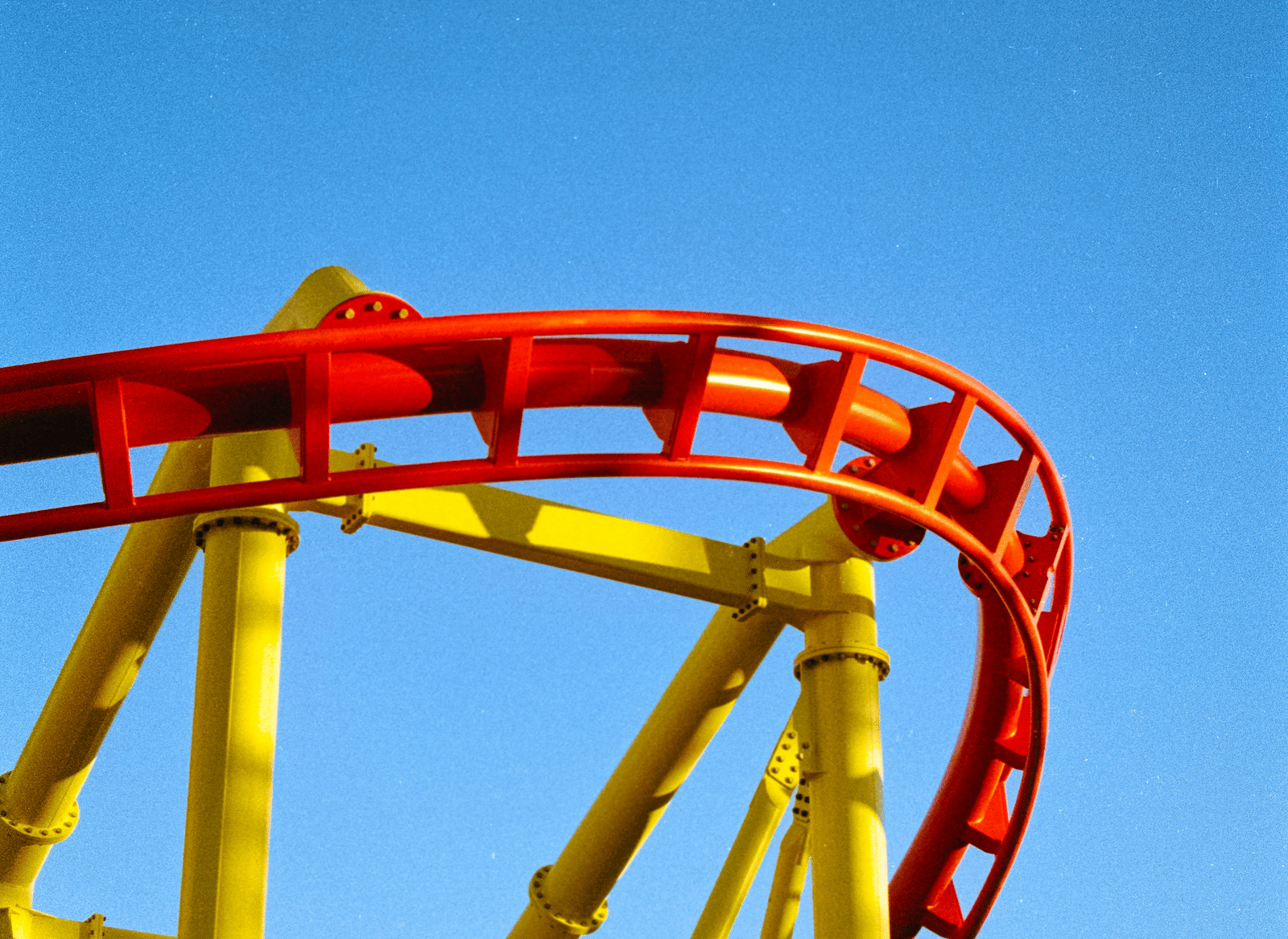 A bright red and yellow roller coaster track curves against a clear blue sky.