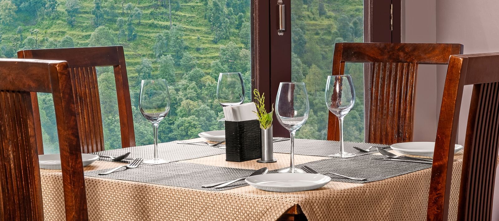 Indoor dining area with a view of terraced hills through large glass windows at BluSalzz Collection - Suvaasa Resort, Ramgarh.