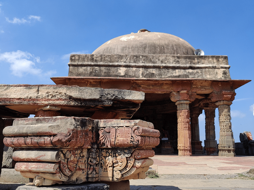 Ancient, weathered stone ruins including a dome and pillars stand beneath a clear, vibrant blue sky.