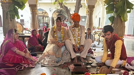 A couple in wedding attire sits at a decorated mandap, surrounded by people and ceremonial items - Fort Barli, Ajmer.