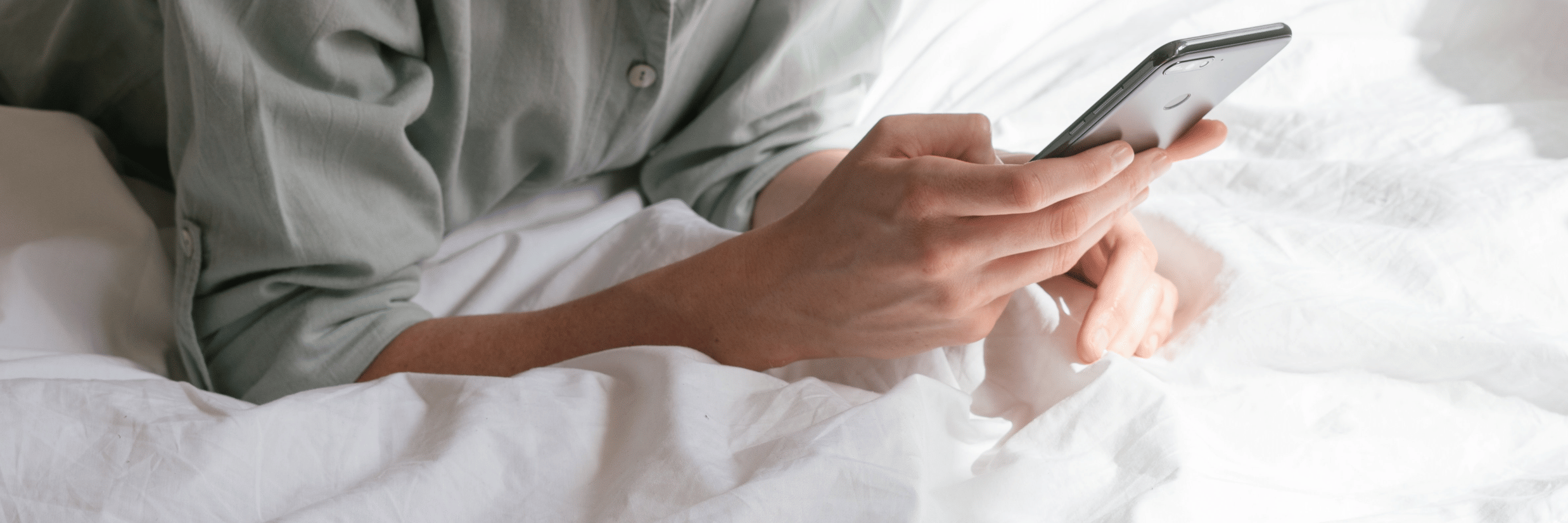 A close up of a woman lying down on her stomach on a bed using her mobile phone.