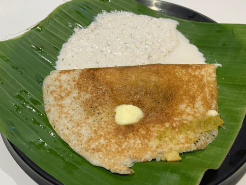 Crispy Benne Dosa served on a banana leaf with coconut chutney.