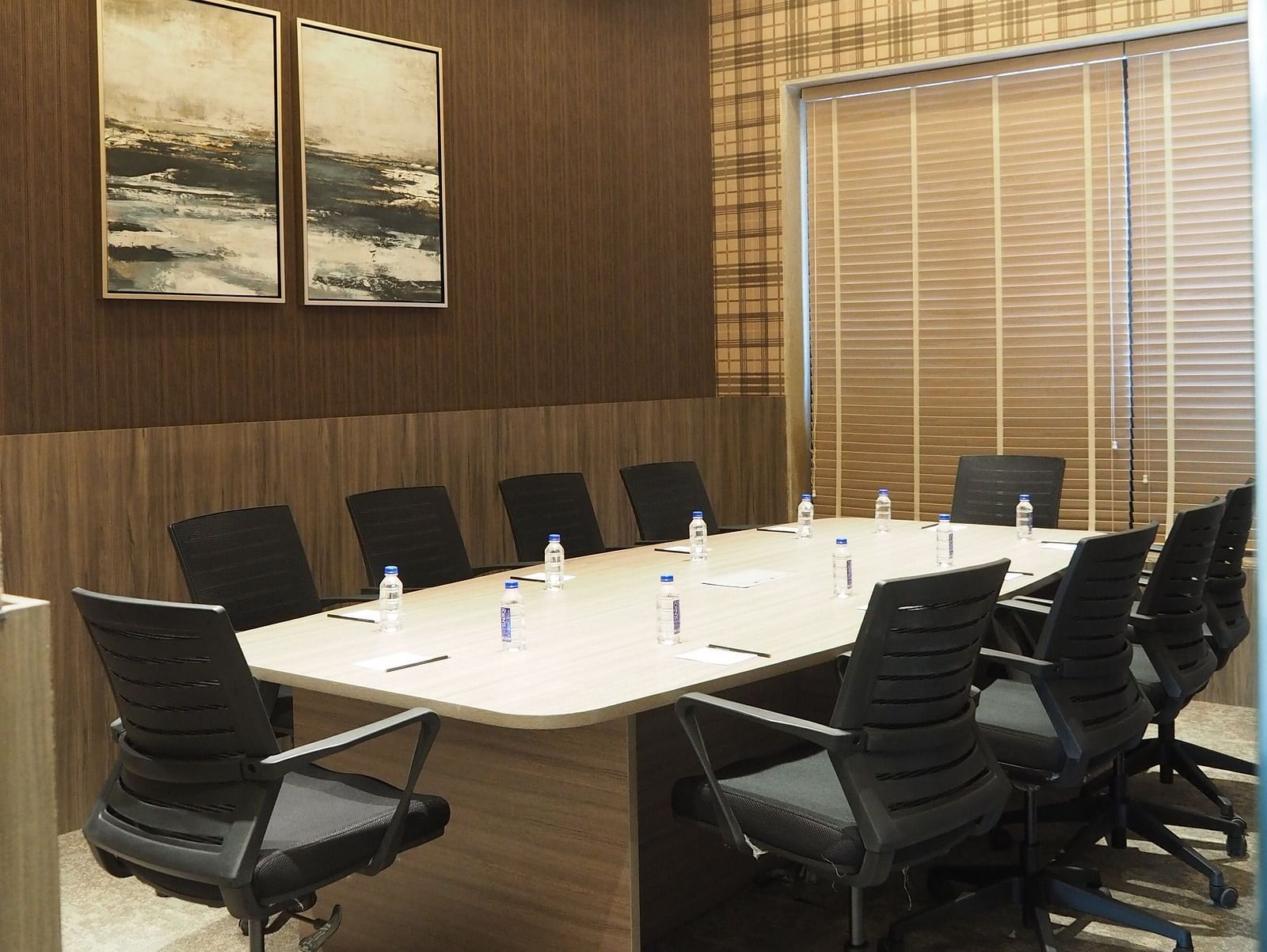 A meeting table with multiple chairs with a dark wall agianst it with a framed picture - Club Charholi, Pune 