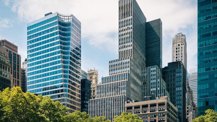 buildings towering over the trees in the foregrounds with white clouds in the background.