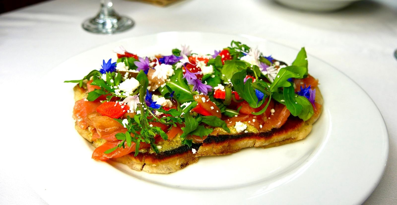 A plated gourmet dish at Shaver Lake Village Hotel topped with vibrant edible flowers, served with a side of soup and wine.