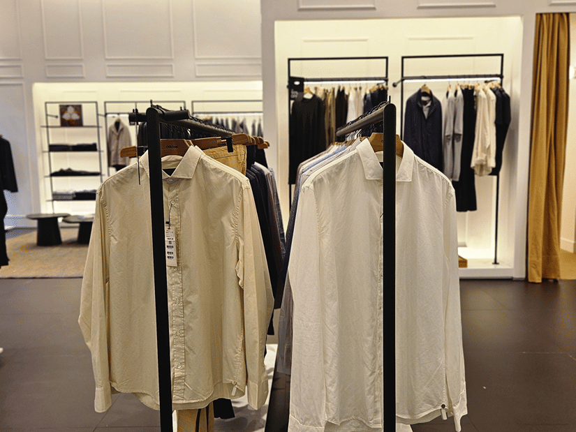 A retail store under warm lighting featuring shirts hanging from the bars