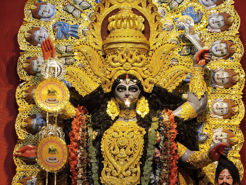 Elaborate golden idol of Goddess Kali adorned with intricate halo details and traditional ornaments against a red backdrop