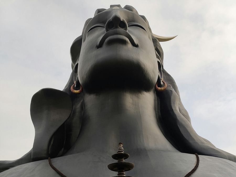 Dark statue of a hindu god with his eyes closed looking up at the sky under a cloudy sky